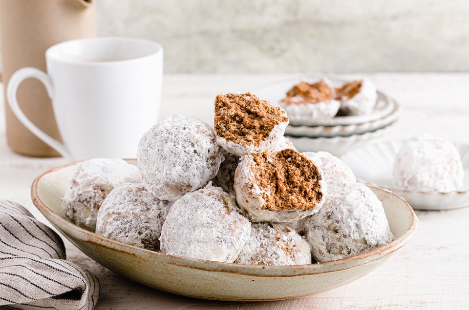 A plate of horchata polvorones coated in sugar next to a hot drink - select to zoom